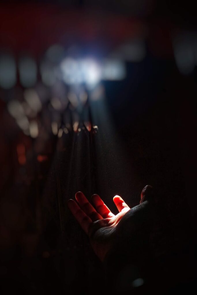 A dramatic image of a hand reaching towards a ray of sunlight in a dark room, symbolizing hope.